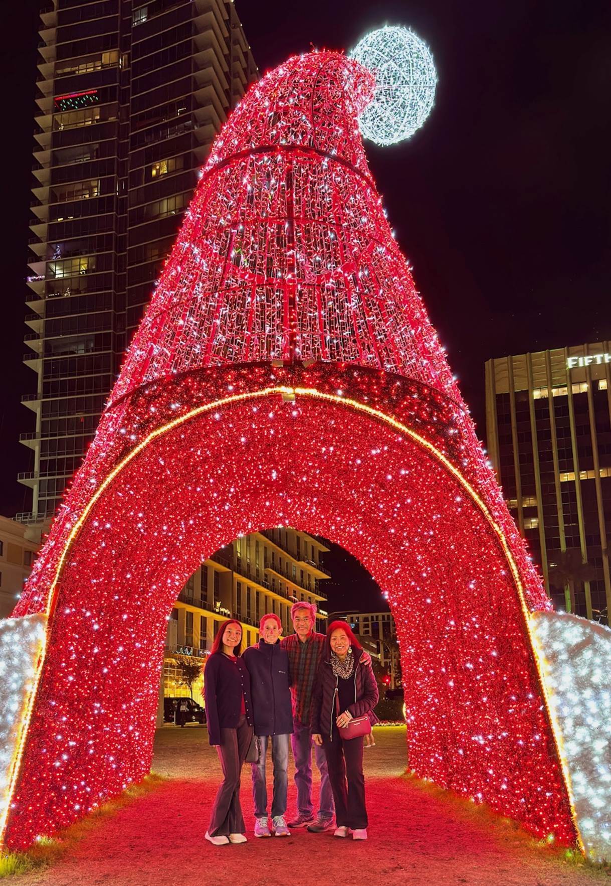 A group of people standing in front of a large red and white christmas tree

Description automatically generated