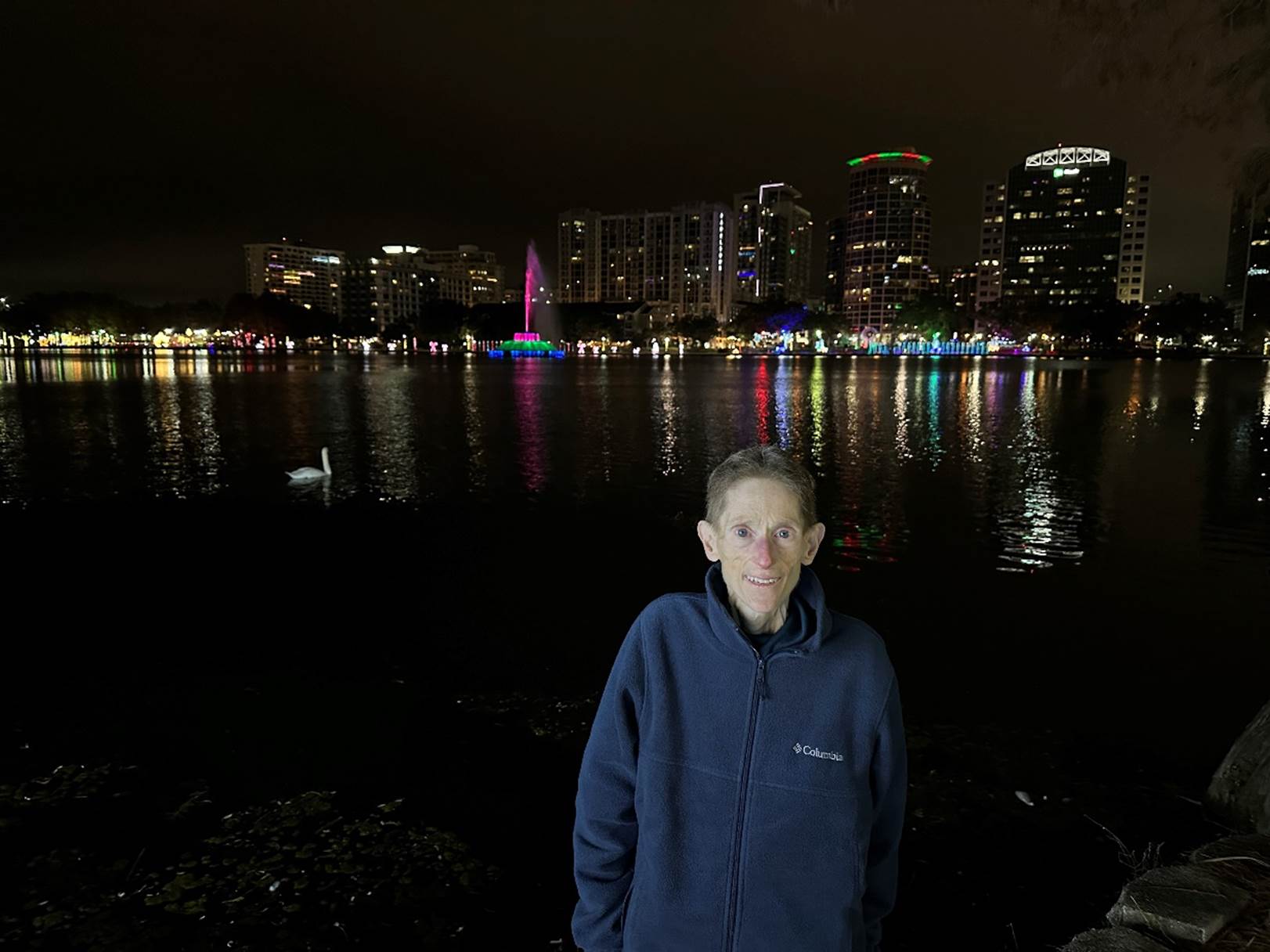 A person standing in front of a body of water with a city in the background

Description automatically generated