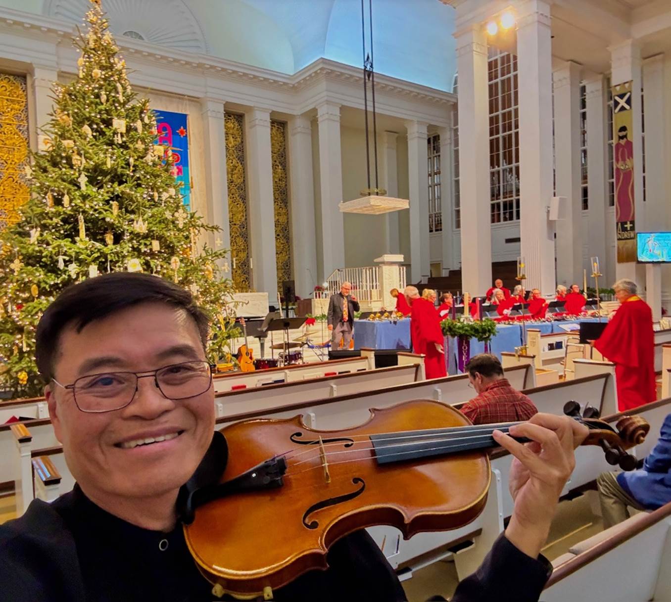 A person holding a violin in front of a christmas tree

Description automatically generated