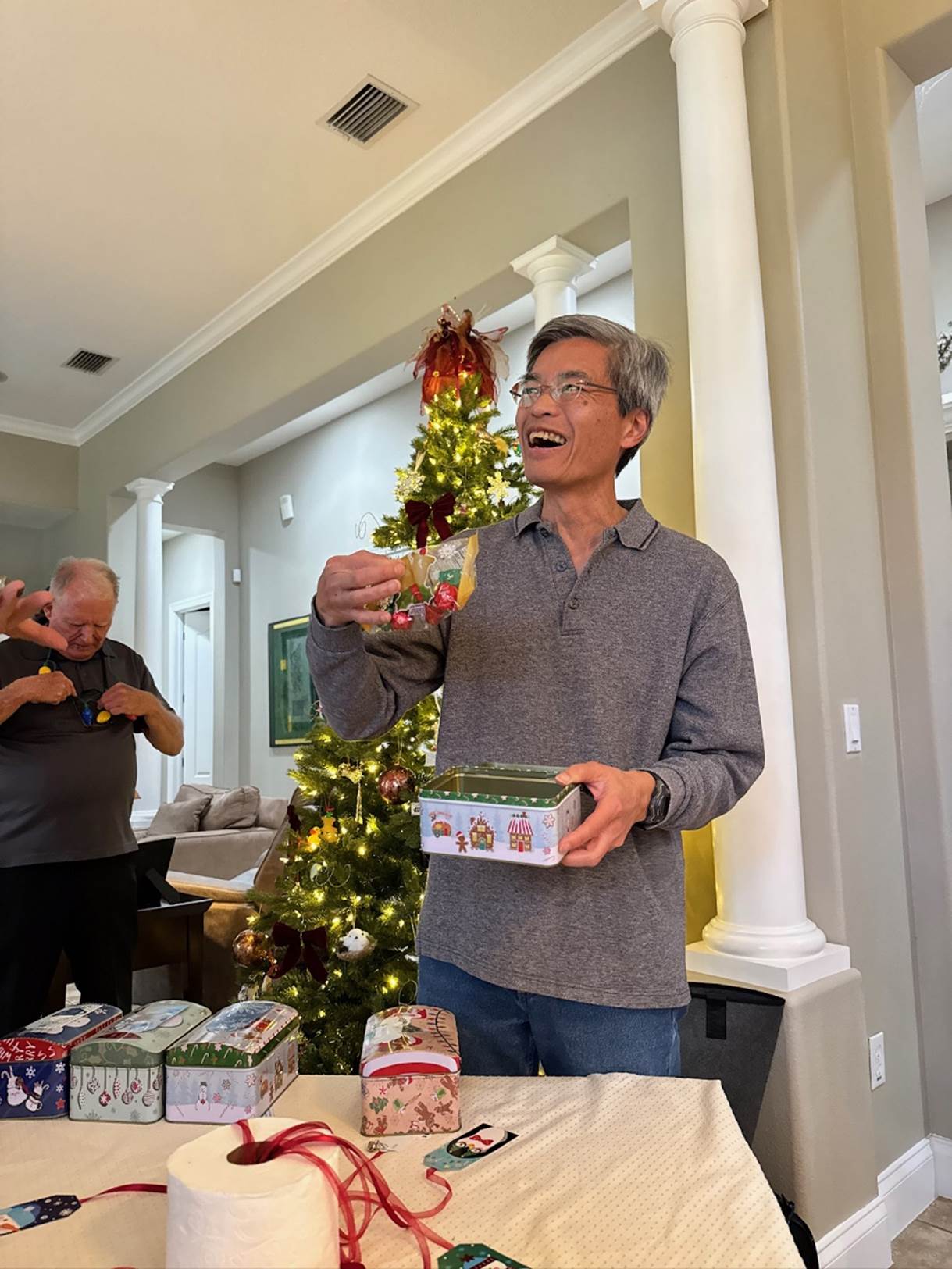 A person holding boxes in front of a christmas tree

Description automatically generated