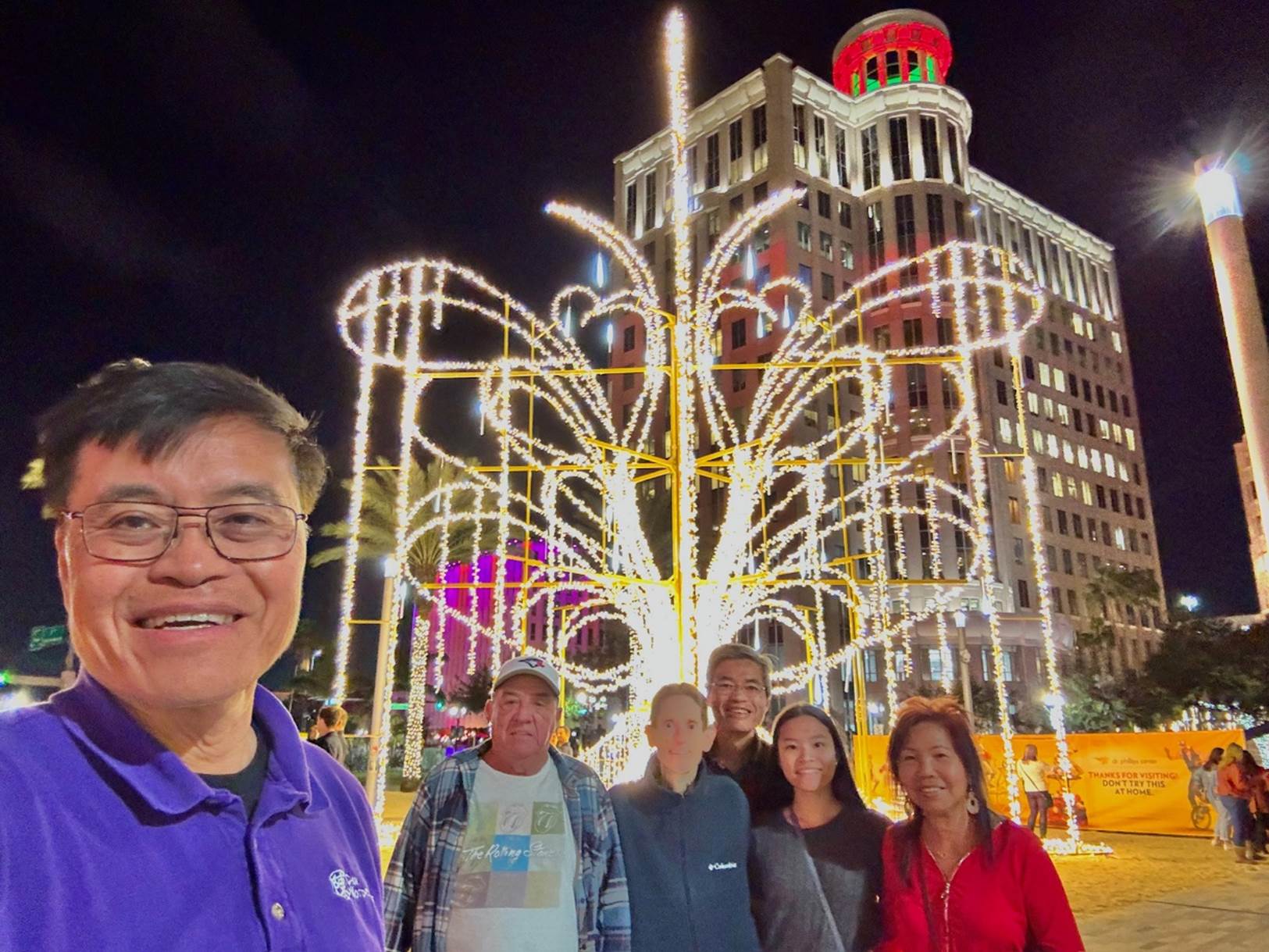 A group of people posing for a photo in front of a lighted tree

Description automatically generated