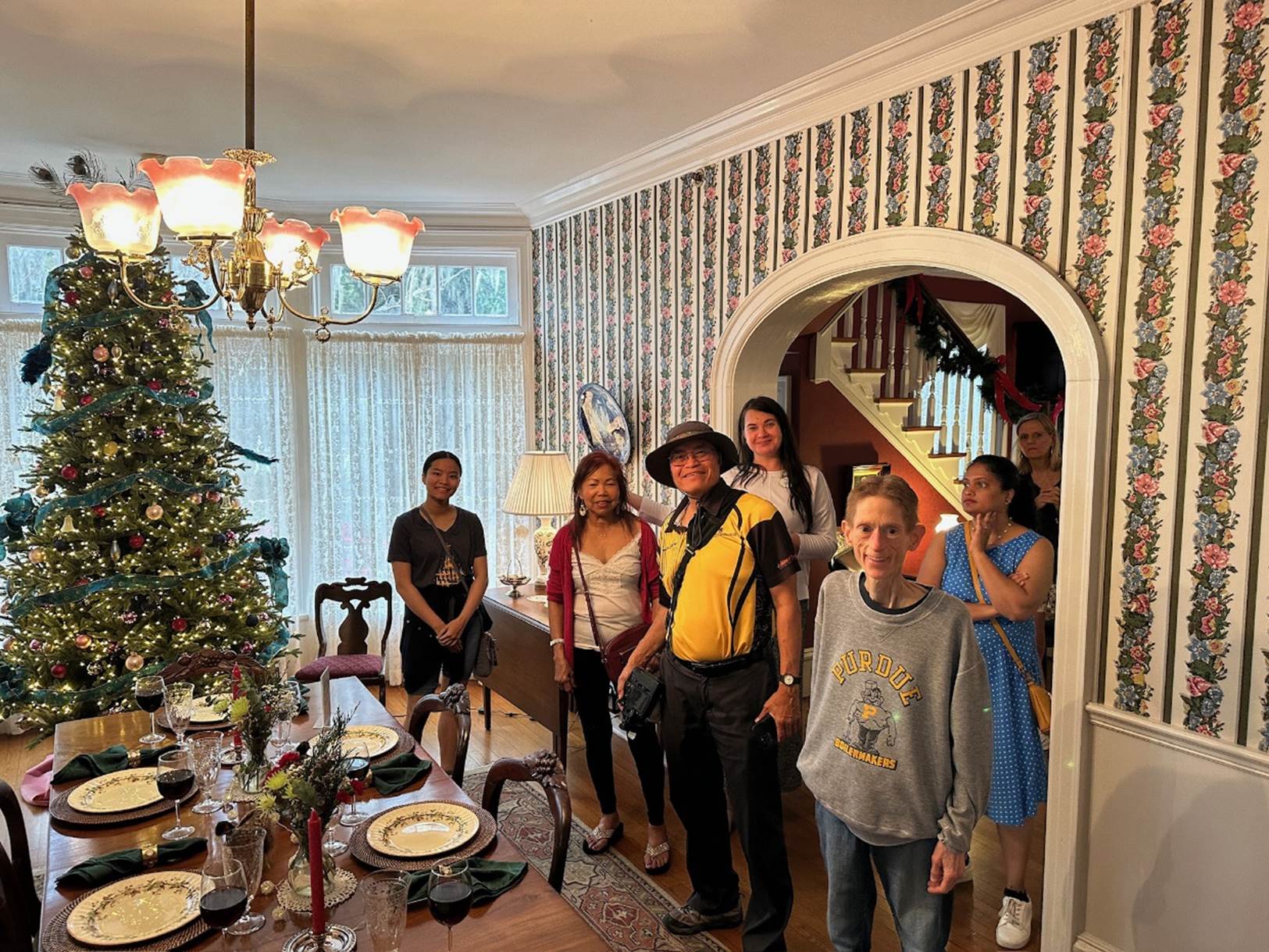 A group of people standing in a room with a christmas tree

Description automatically generated